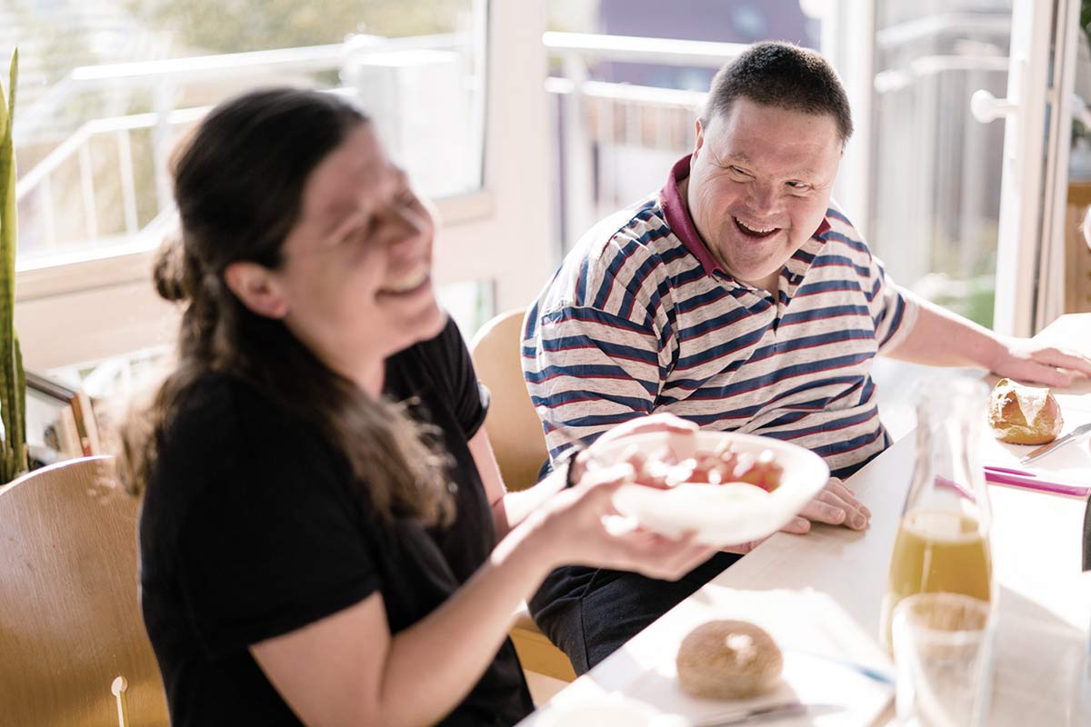 Zwei Menschen sitzen lachend am Frühstückstisch
